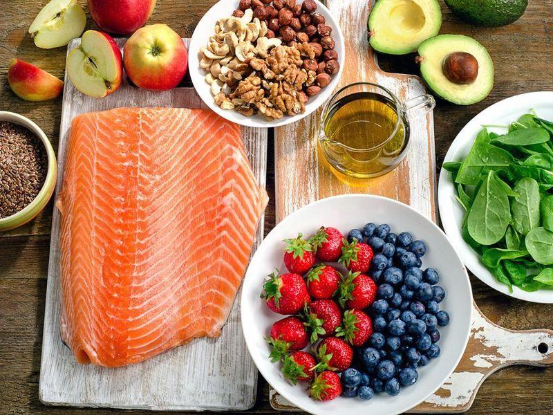 a wooden table laden with many health foods, including salmon, berries, greens, and oats